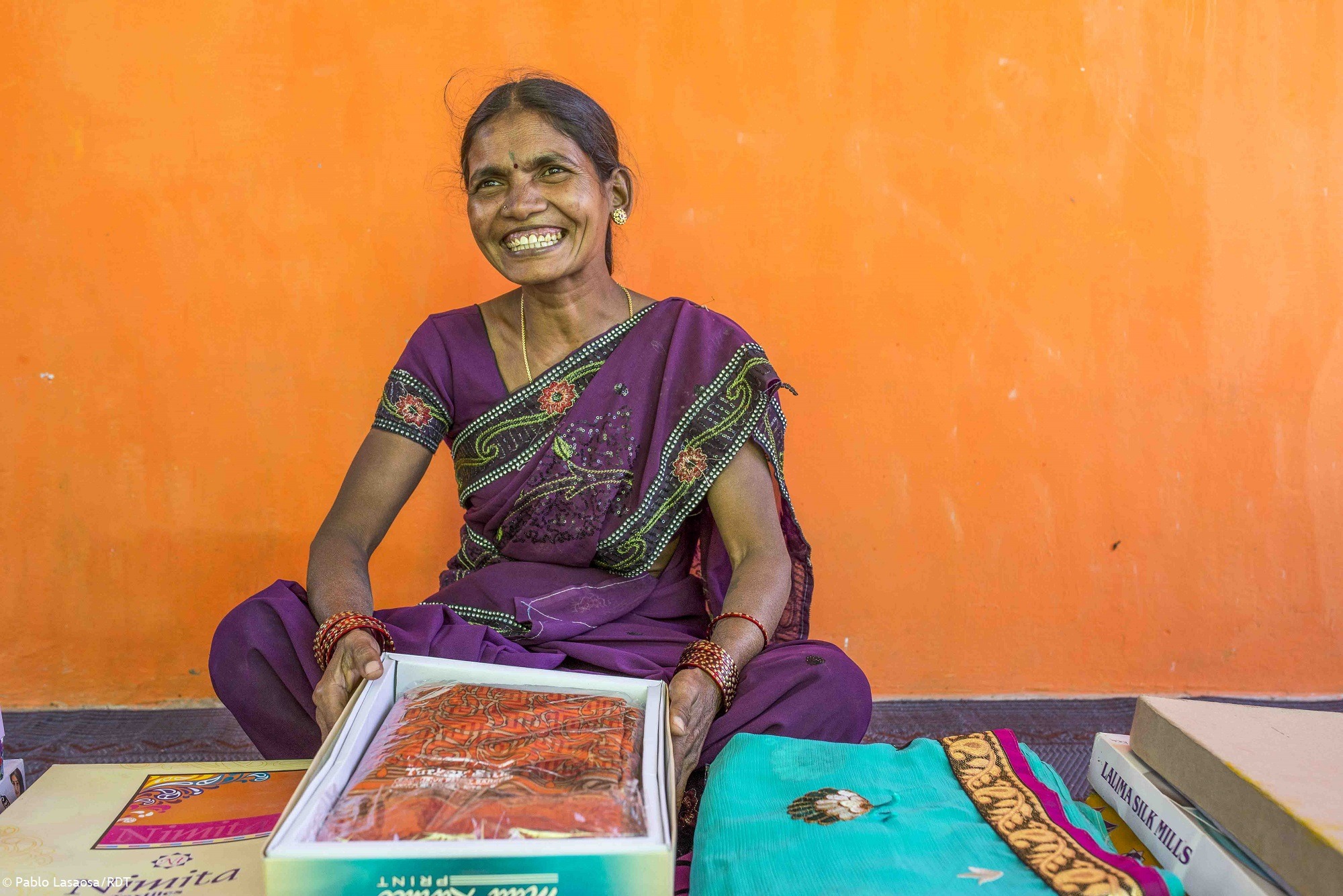 Frau in Indien mit lila Sari vor oranger Wand.