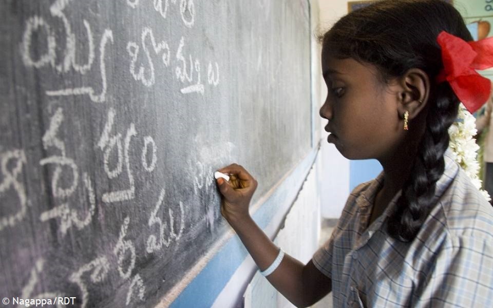 Mädchen schreibt mit Kreide an eine Schultafel in Indien. Mit Stiftungsschulen Alphabetisierung in Indien fördern